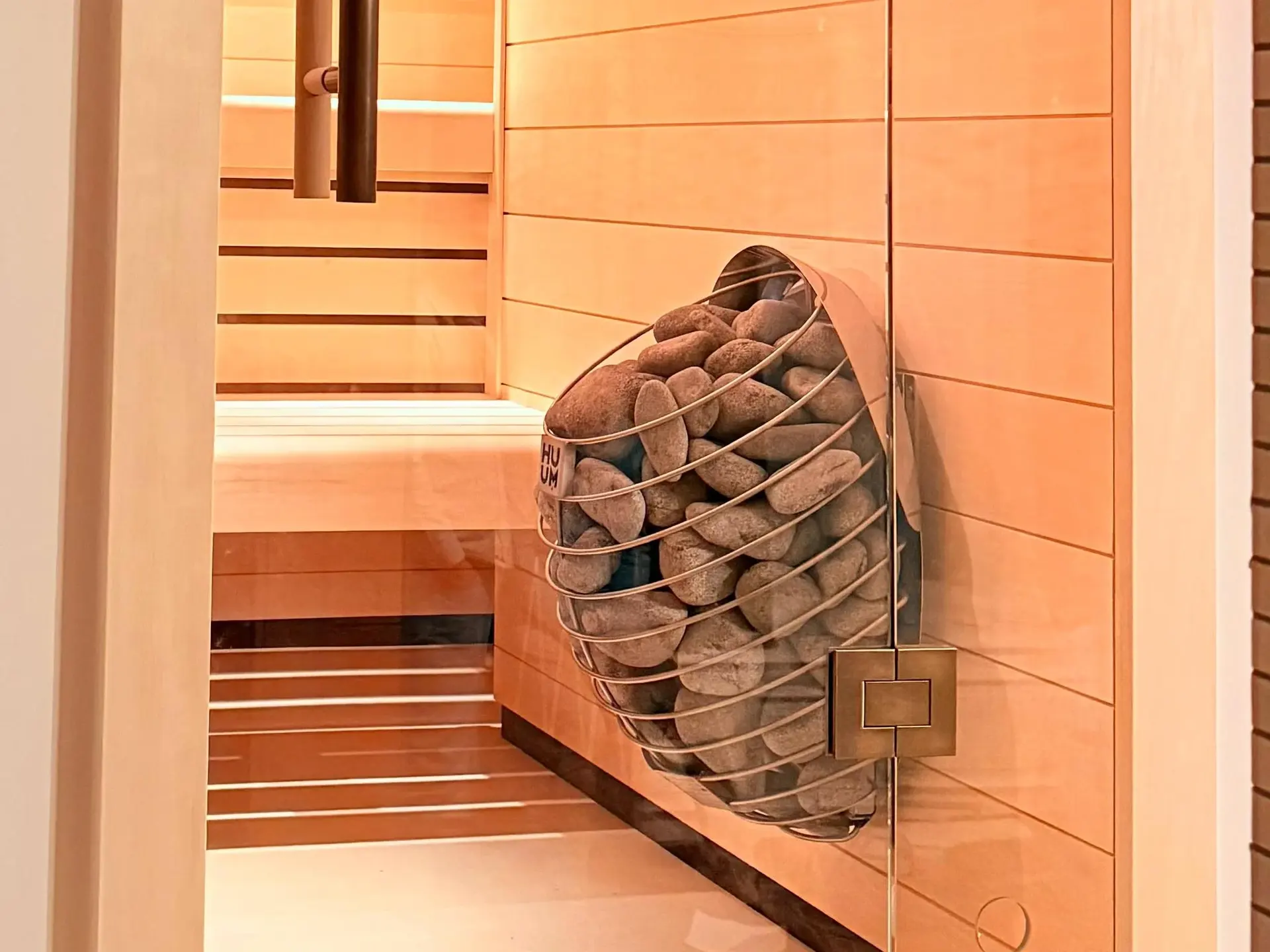 Detail of a bespoke sauna: a HUUM Drop heater with sauna stones against pale wood