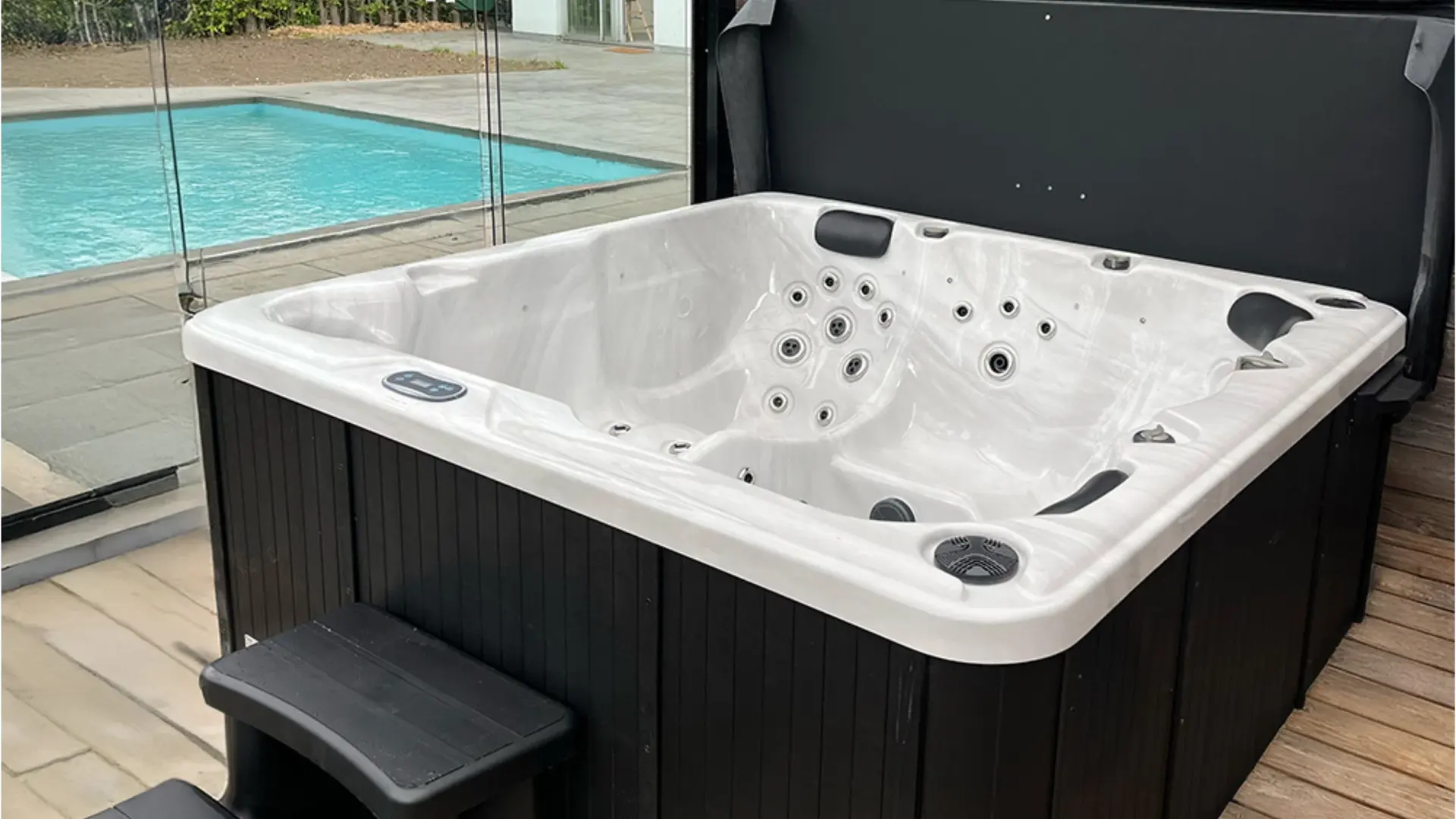 Net geplaatste spa met witte kuip en zwarte omkasting op een houten vlonder, de cover opengeklapt
