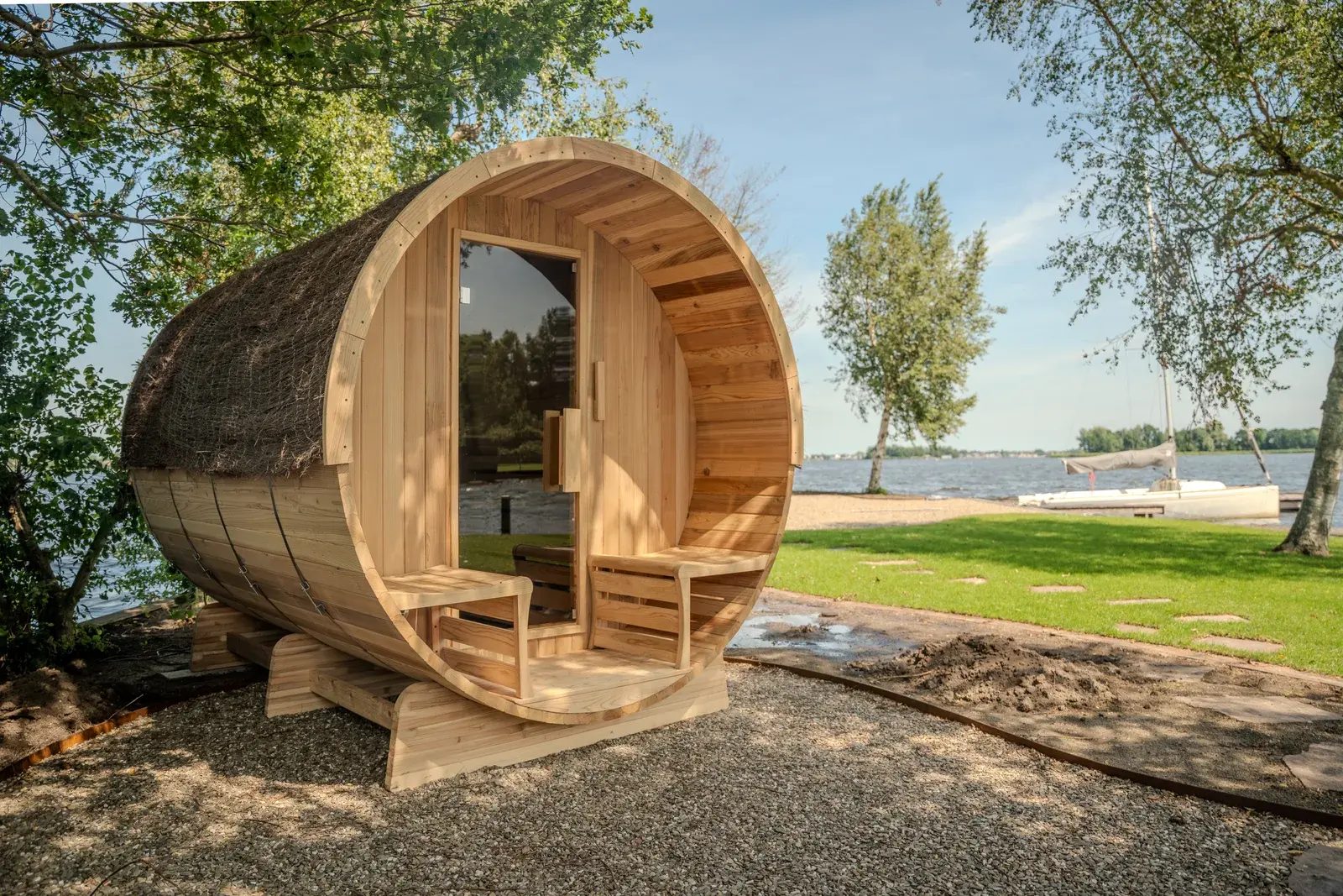 Barrel sauna at the water’s edge with a sailboat behind