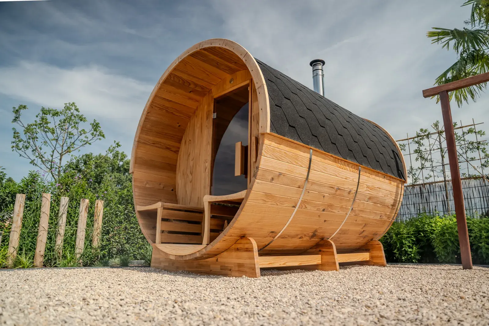 Side view of a barrel sauna with a black roof in a garden