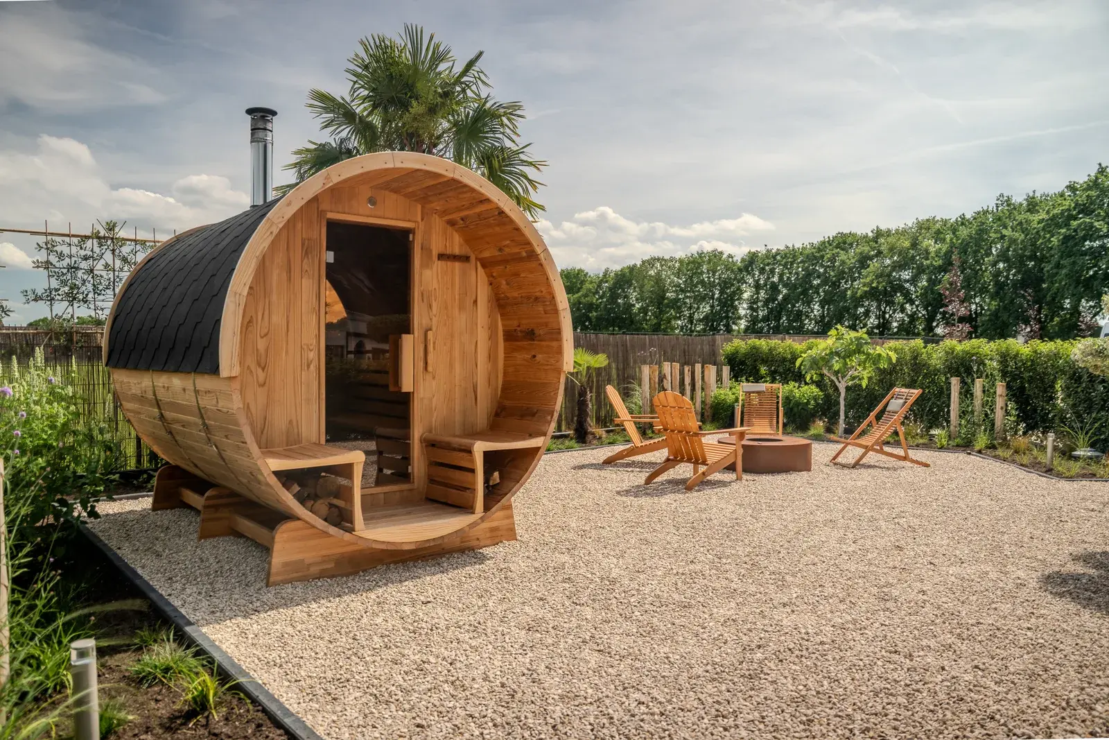 Barrel sauna in a garden with loungers and a fire bowl