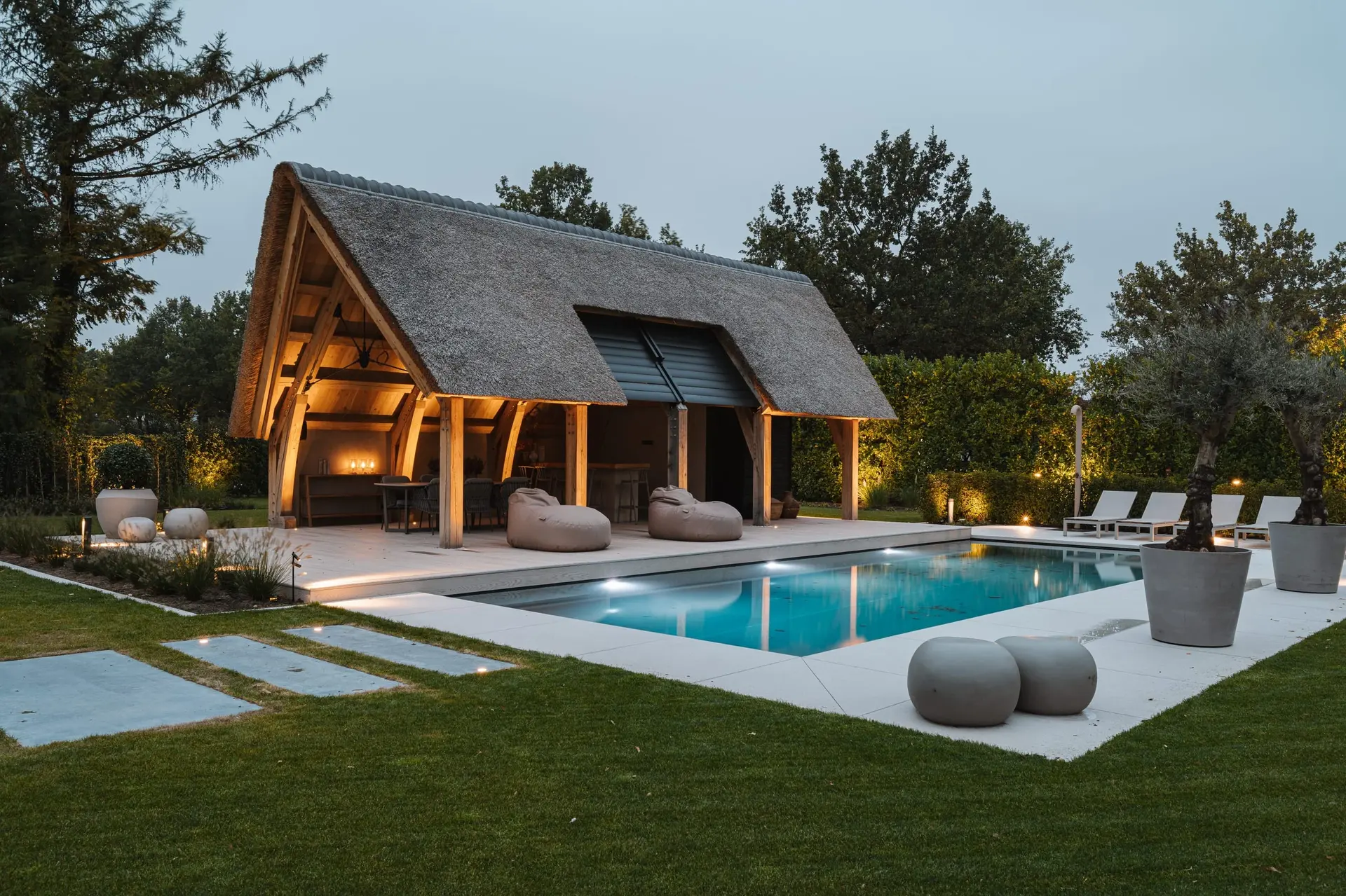 Tuin met verlicht poolhouse en zwembad in de avondschemering